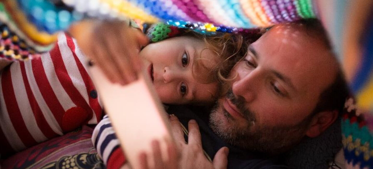 Male and child looking at phone screen under a blanket